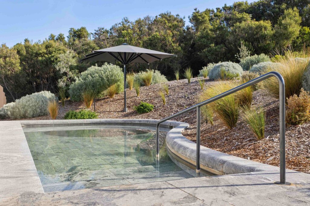 The curved stone coping of a thermal pool at Alba, supplied by Eigen Stones, set within a beautiful, natural bushland environment.