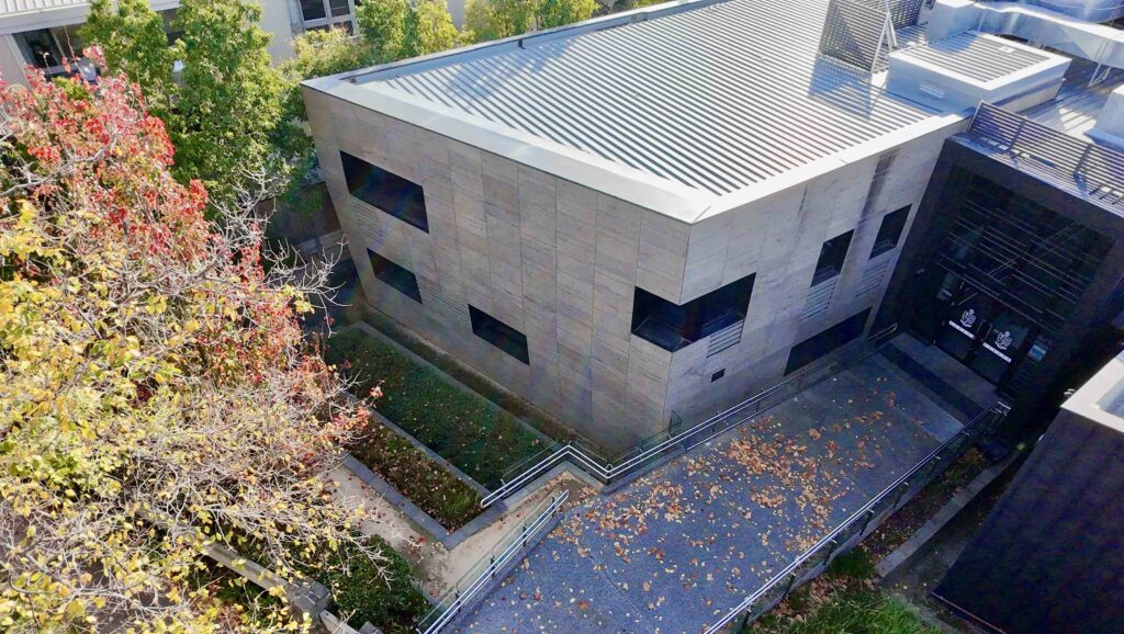A high-angle view of a monolithic stone-clad building at St Kevin's, surrounded by lush trees and a paved walkway from Eigen Stones.