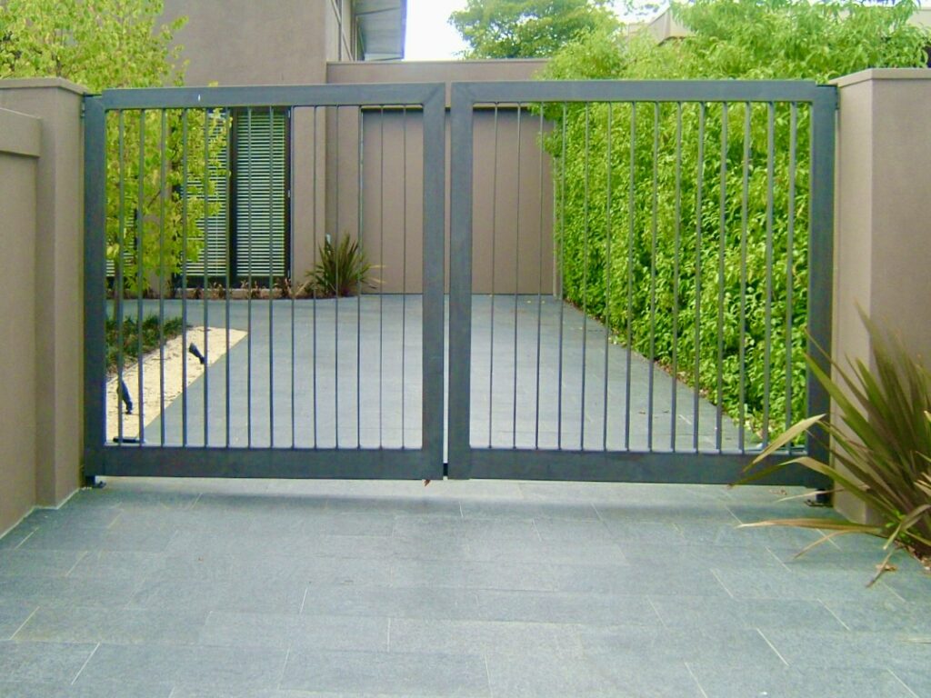 A modern, dark stone paver driveway, supplied by Eigen Stones, leading to a sleek metal security gate at a contemporary home.