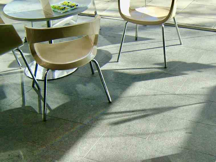 Sunlight casts shadows across the deep-toned, polished stone floor at 571 Fitzroy Street, where modern chairs are placed, with flooring supplied by Eigen Stones.