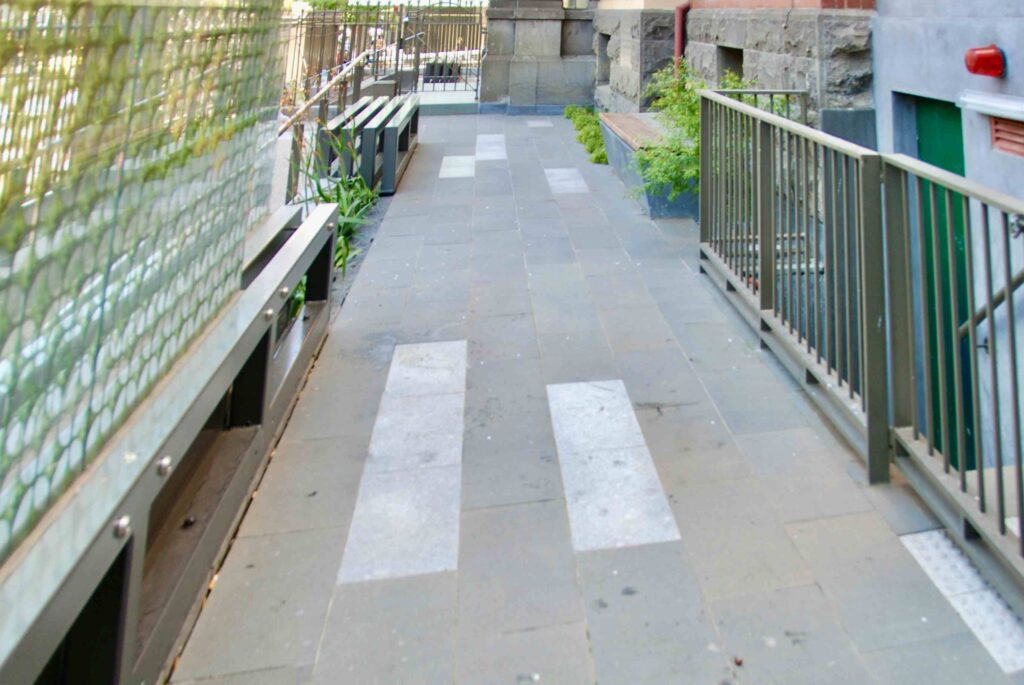 The long, patterned stone laneway at the Victorian Women's Centre, featuring integrated seating and planters, with all pavers supplied by Eigen Stones.
