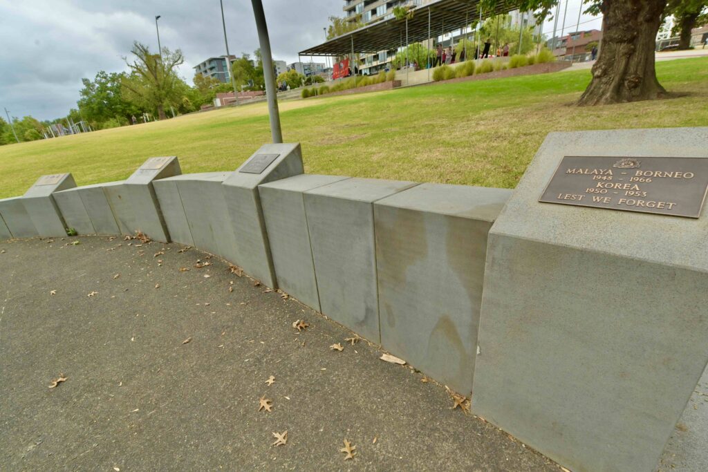 A low-angle view of the curved concrete memorial wall at Box Hill, featuring bronze plaques, with stone supplied by Eigen Stones.