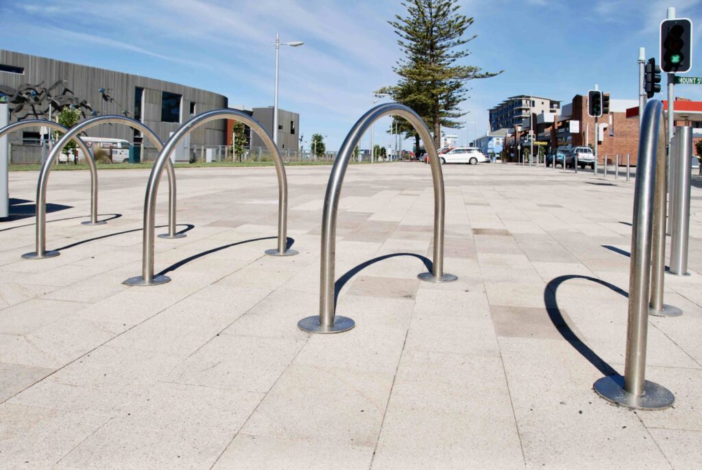 Modern, curved stainless steel bike racks stand on the stone-paved Bernie Waters plaza, with the durable paving supplied by Eigen Stones.