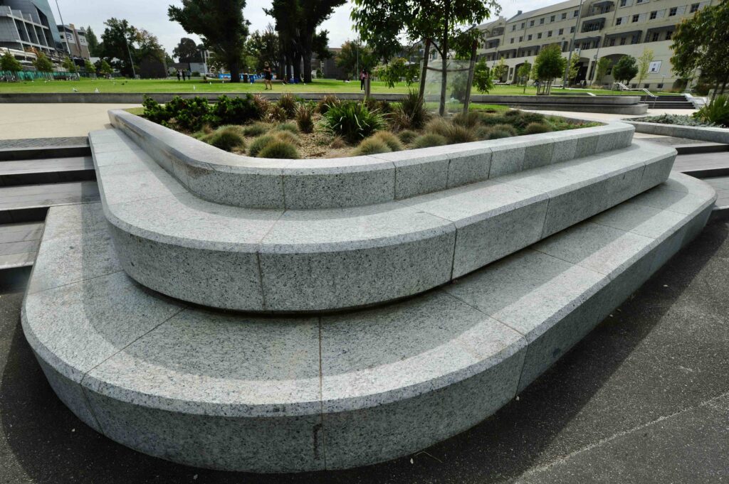 A close-up of the sculptural, multi-tiered stone seating at Uni Square, showcasing the precise curves and speckled finish of the stone supplied by Eigen Stones.