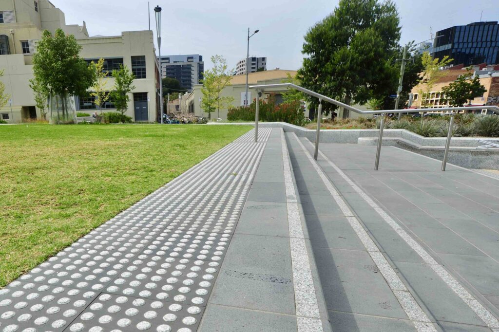 An accessible stone staircase at Uni Square, bordered by a green lawn and featuring integrated tactile pavers for safety, with all stone supplied by Eigen Stones.
