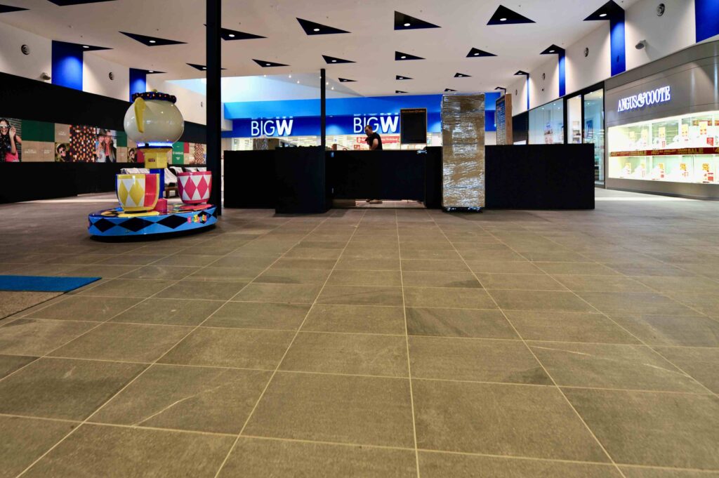 The spacious central court of Craigieburn Shopping Centre, featuring a broad expanse of dark stone flooring from Eigen Stones, leading towards a Big W store.