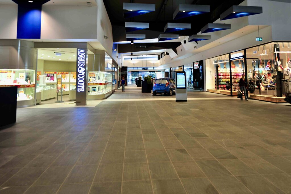 The main thoroughfare of Craigieburn Shopping Centre, showing the extensive dark stone flooring supplied by Eigen Stones, leading past various retail storefronts.