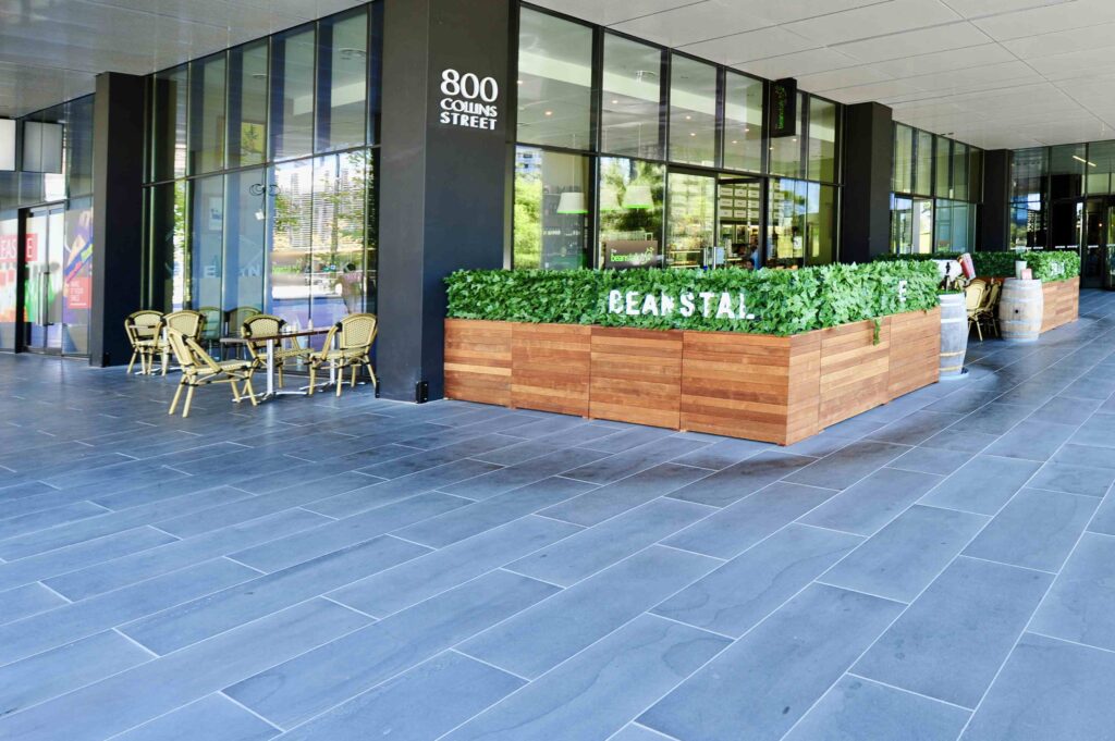 The sleek, dark stone forecourt of the Docklands Myer building at 800 Collins Street, creating a sophisticated entrance for a cafe. Stone supplied by Eigen Stones.