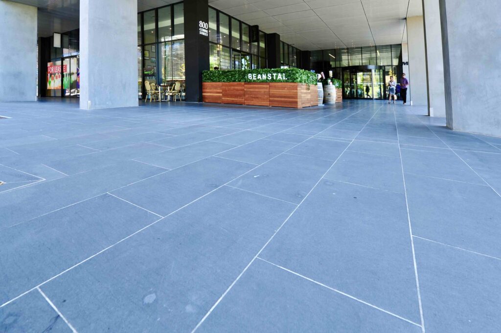 A wide view of the expansive, sheltered walkway at the Docklands Myer headquarters, paved with large-format dark stone from Eigen Stones.