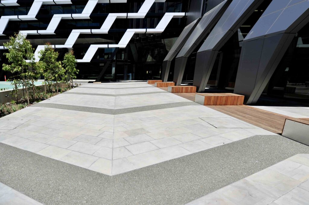 The modern, multi-story ACU building with its glass and concrete facade, rising above the stone-paved public square supplied by Eigen Stones.