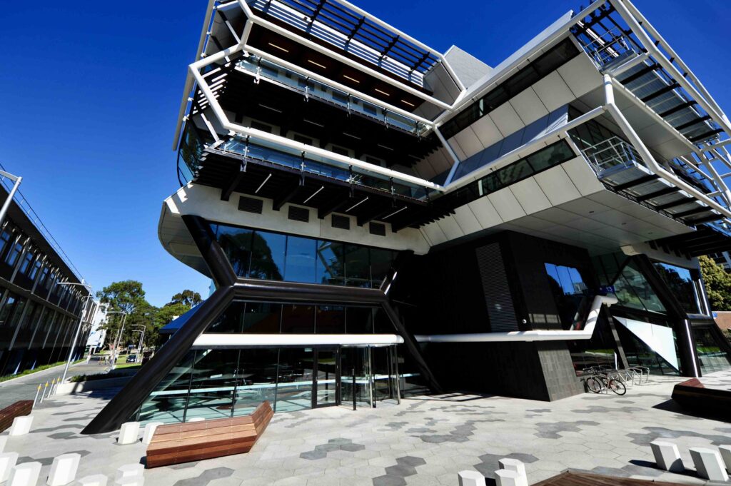 A perspective view of the chevron-patterned stone forecourt at Kangan Institute, with the bold black-and-white facade in the background. Stone supplied by Eigen Stones.